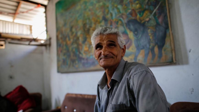 نقاش فلسطینی فتحی غبن در خانه خود نشسته است و نقاشی معروف خود در نبرد عین جالوت در پس زمینه در این عکس که در 11 ژوئیه 2015 گرفته شده است. - معتز علارج